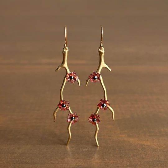Gold branch-like earrings with red flower charms on a brown background