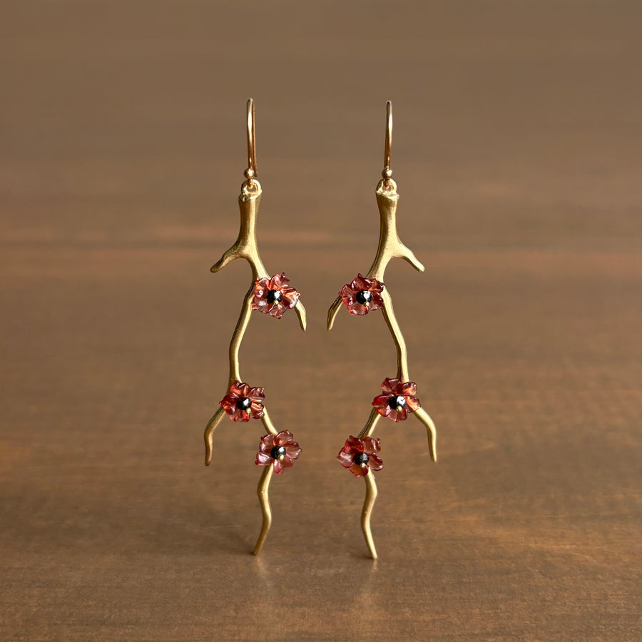 Gold branch-like earrings with red flower charms on a brown background