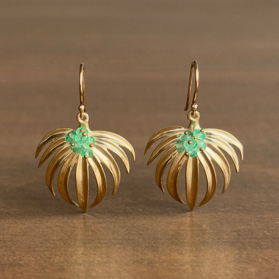 Pair of gold earrings with green gemstones on a brown background