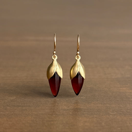 Gold earrings with red gemstones on a brown background