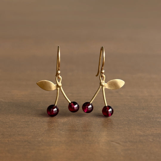 Gold earrings with red gemstones on a brown background