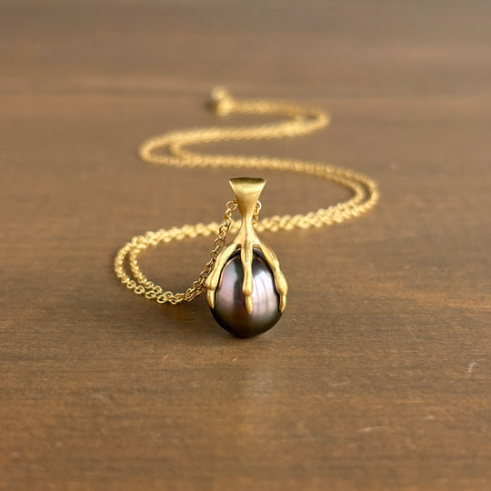 Gold necklace with a black pearl pendant on a wooden surface