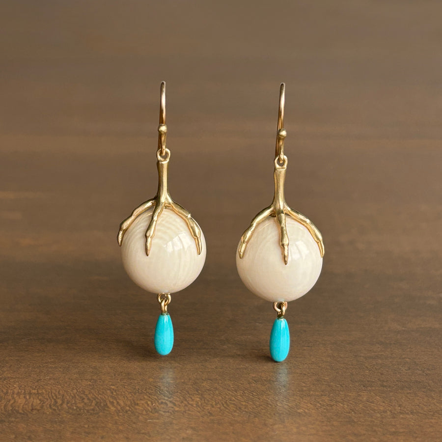 Pair of earrings with gold accents, white stones, and turquoise drops on a brown background