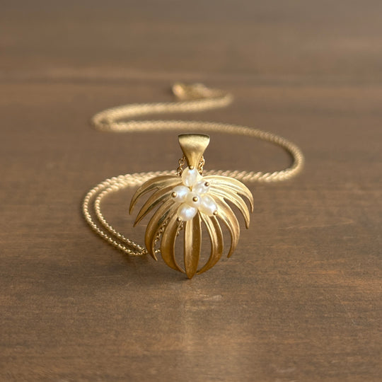 Gold necklace with a leaf-shaped pendant on a brown surface