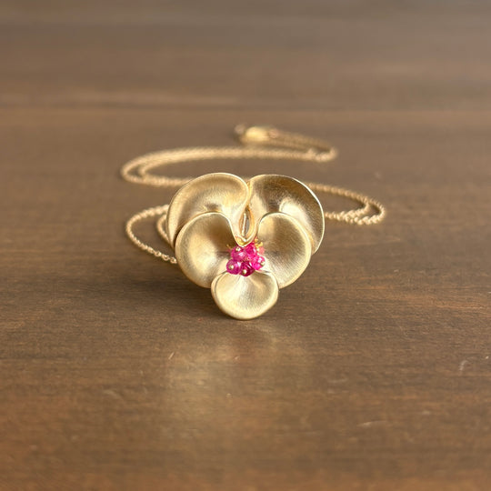 Gold flower-shaped pendant with pink gemstones on a wooden surface