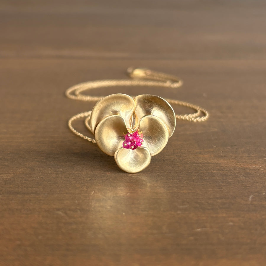 Gold flower-shaped pendant with pink gemstones on a wooden surface