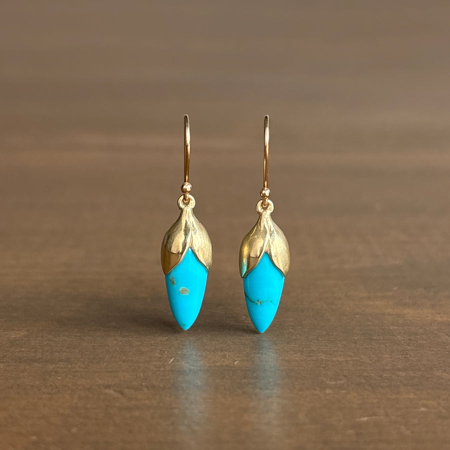 Gold and turquoise earrings on a brown surface