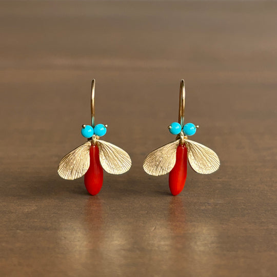 Pair of earrings with gold leaf-like designs, red beads, and turquoise stones on a brown background.