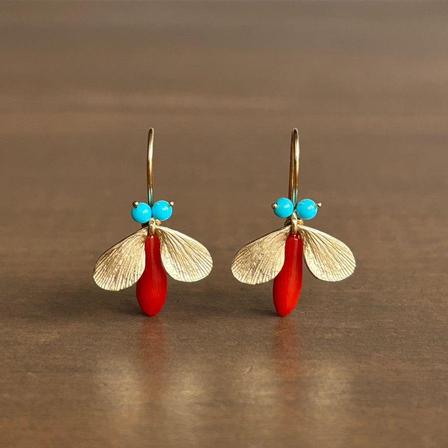 Pair of earrings with gold leaf-like designs, red beads, and turquoise stones on a brown background.