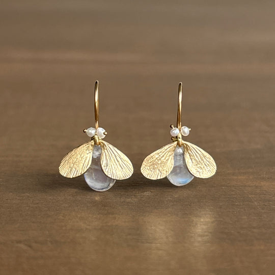 Gold wing-shaped earrings with clear stones on a brown background