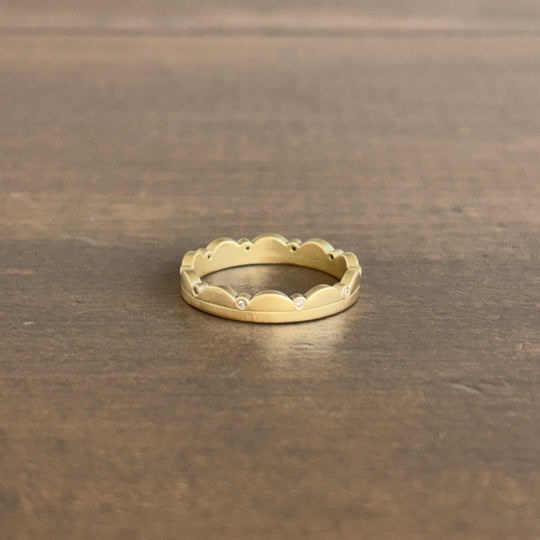 Gold ring with scalloped edge and small diamonds on a brown surface