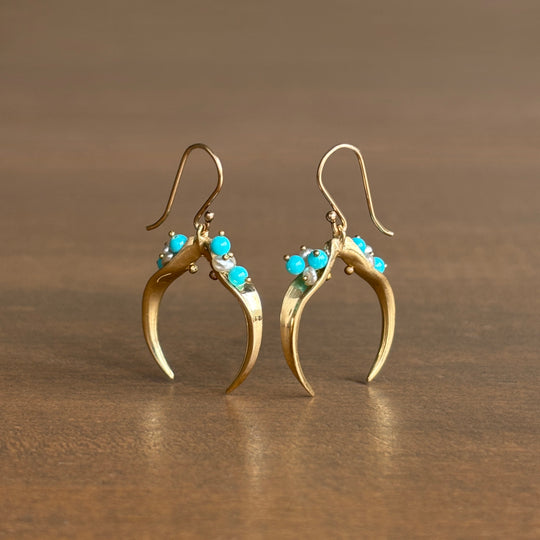 Gold earrings with turquoise stones on a brown background