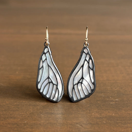 Pair of silver wing-shaped earrings on a wooden surface
