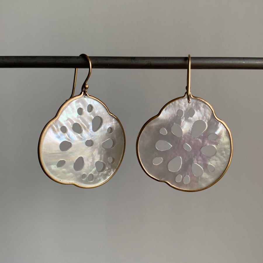 Pair of patterned earrings hanging on a rod against a neutral background