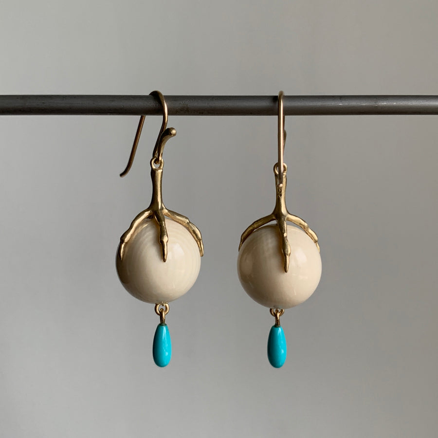 Pair of earrings with gold hooks, beige spherical stones, and turquoise drops on a gray background