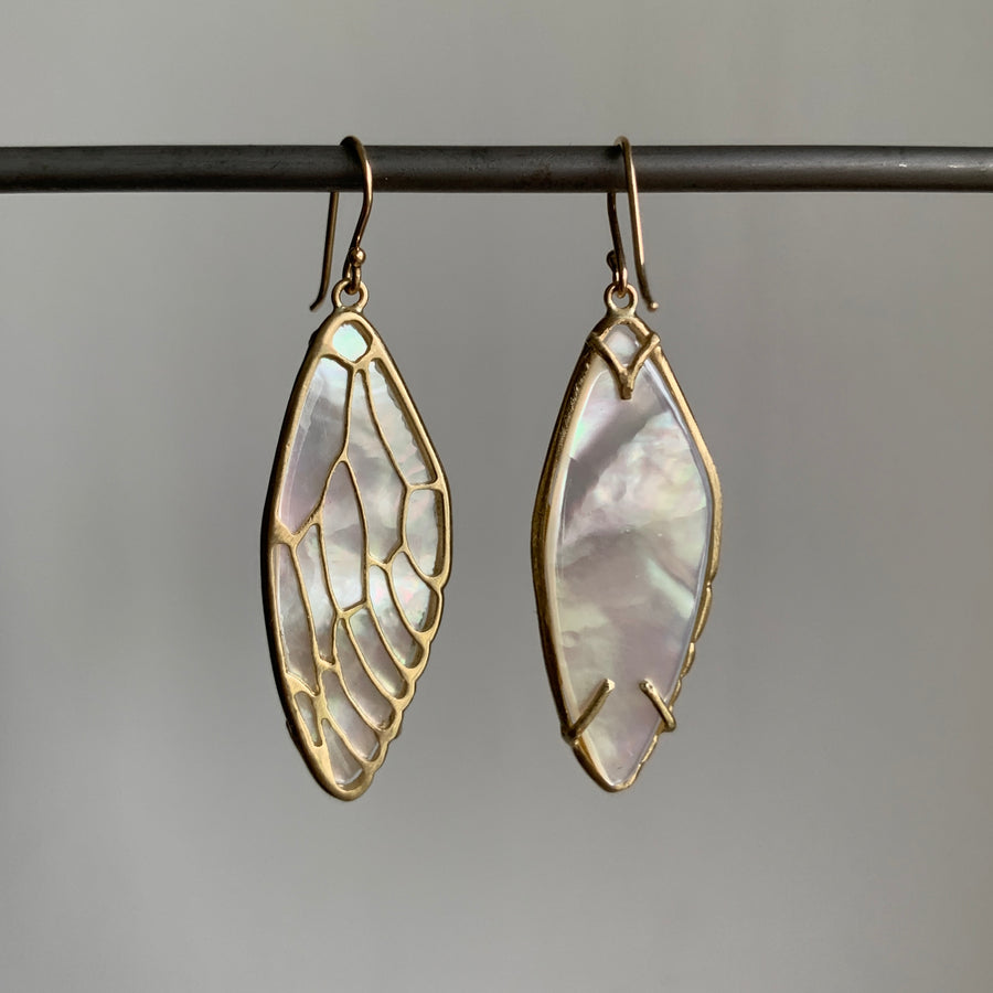 Gold-framed earrings with a mother-of-pearl design on a gray background