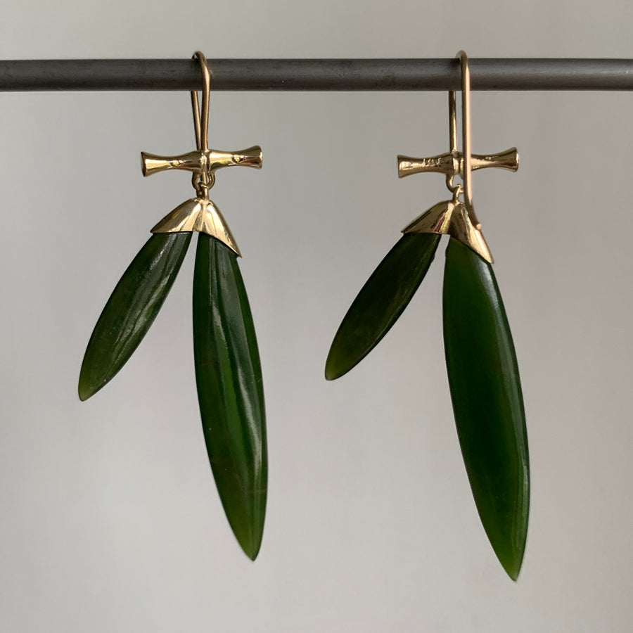 Pair of earrings with gold tops and green leaves on a gray background