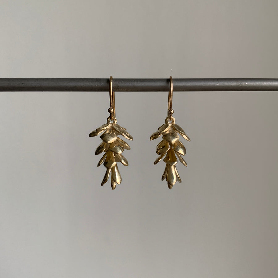 Gold leaf-shaped earrings hanging on a rod against a neutral background