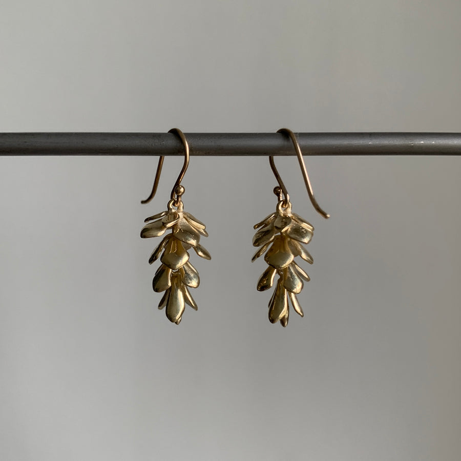 Gold leaf-shaped earrings on a gray background