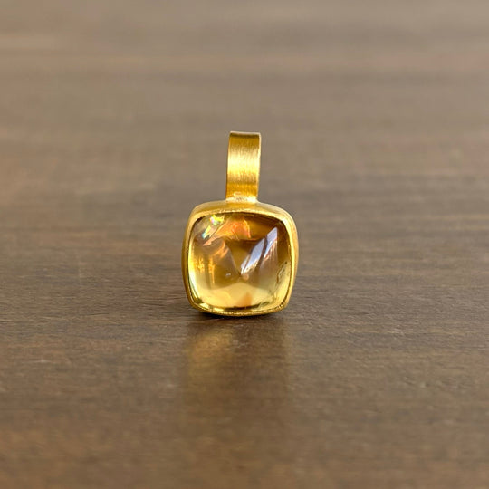 Gold pendant with a clear gemstone on a wooden surface