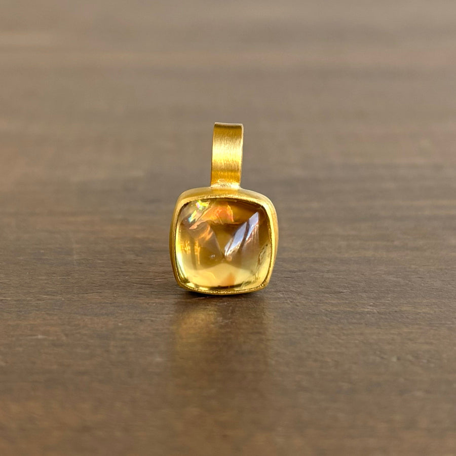 Gold pendant with a clear gemstone on a wooden surface