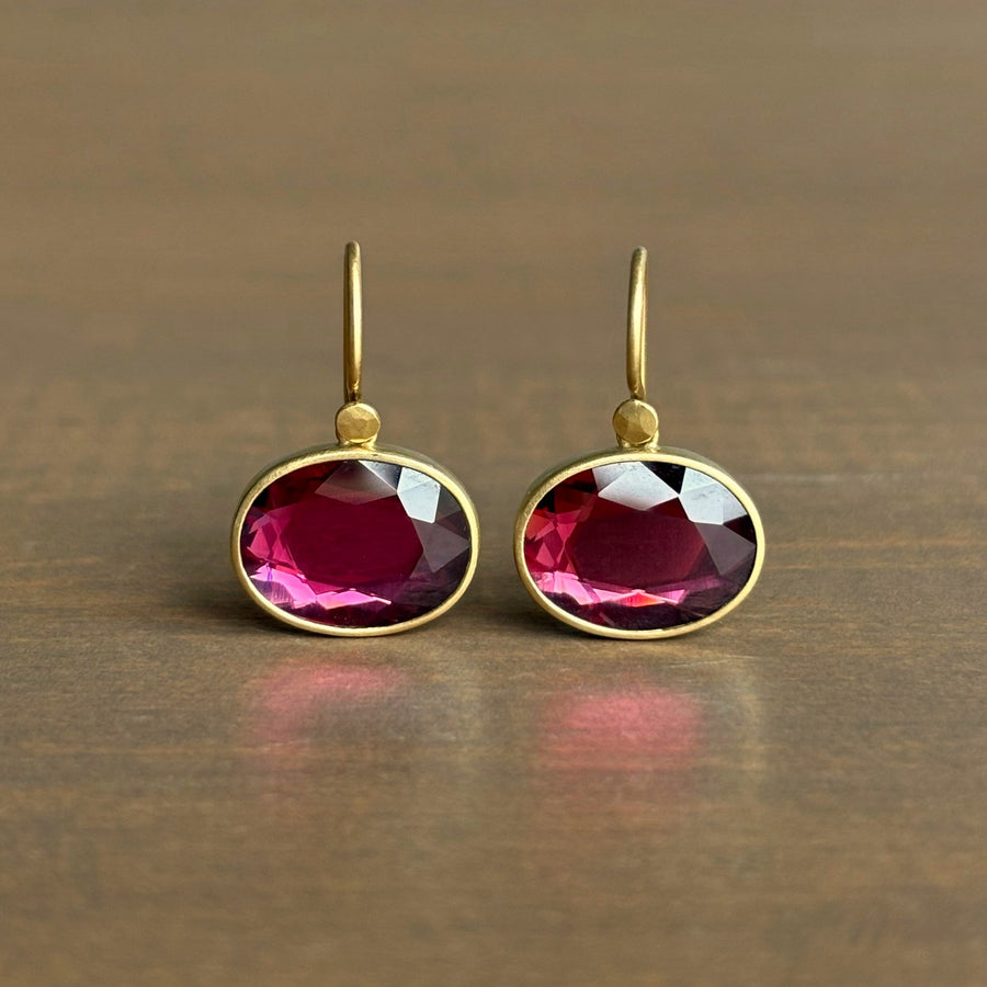 Gold earrings with red gemstones on a wooden surface