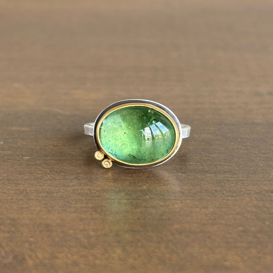 Ring with a green gemstone and diamonds on a wooden surface