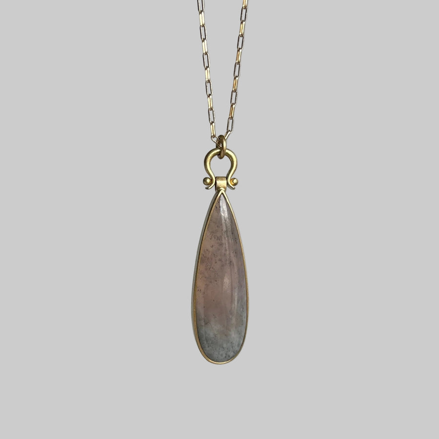 Teardrop-shaped pendant on a chain against a gray background