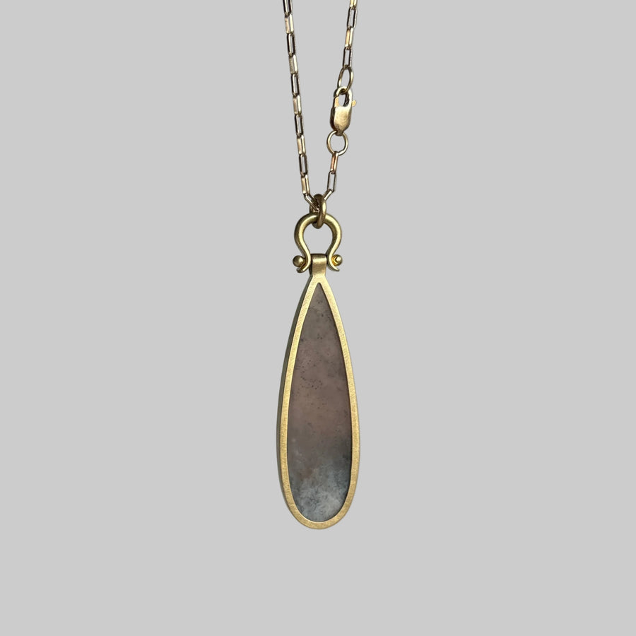 Teardrop-shaped pendant on a chain against a gray background