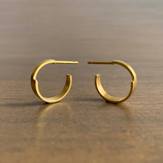 Gold hoop earrings on a reflective surface with a neutral background