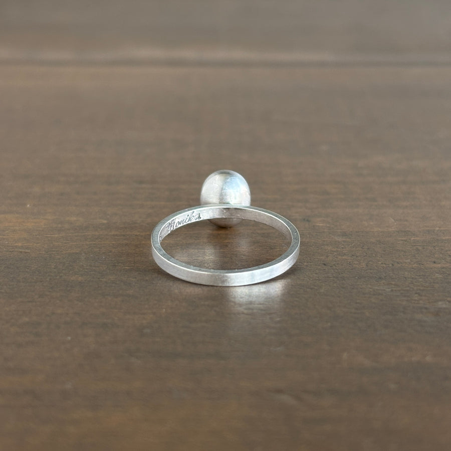 A minimalist sterling silver band ring with a small gemstone displayed on a dark brown wooden surface.