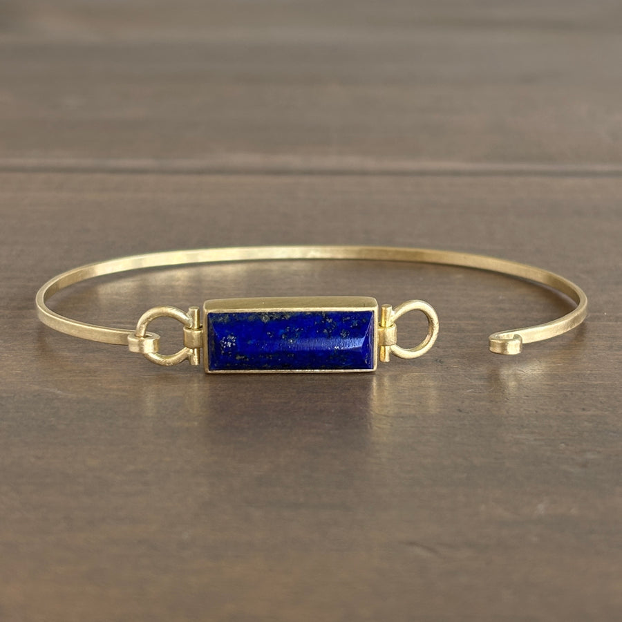 Gold bracelet with a blue stone on a wooden surface