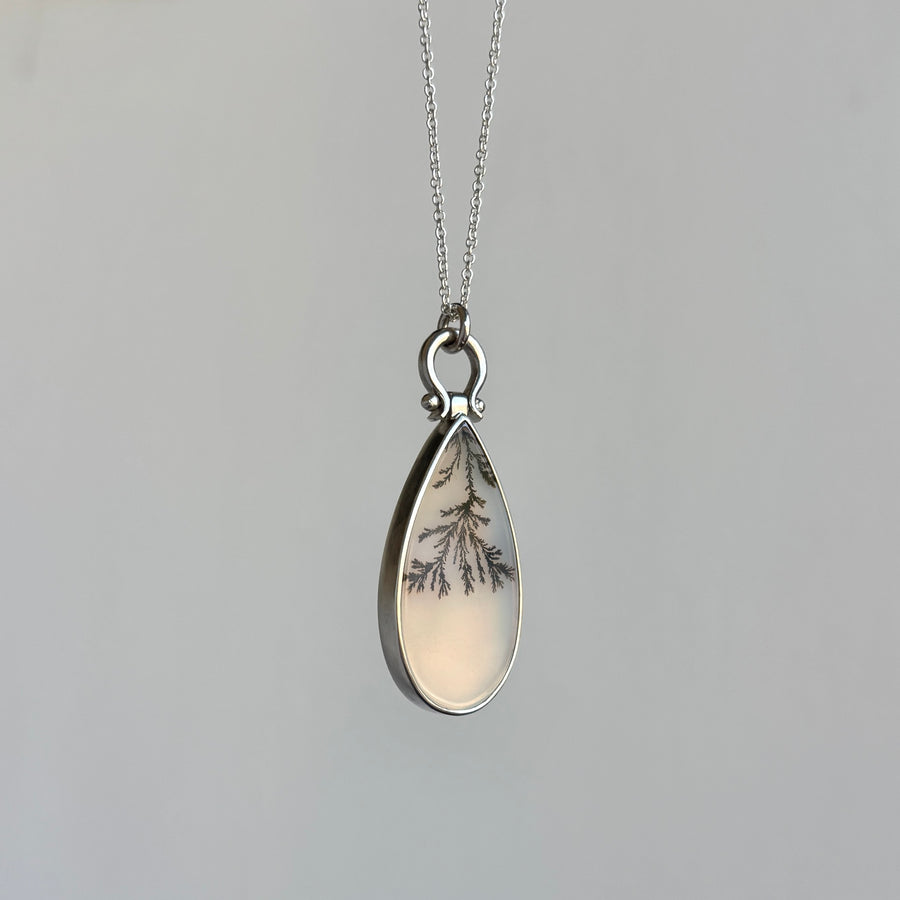 Teardrop-shaped pendant with tree design on a gray background