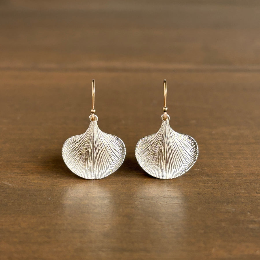 Pair of silver fan-shaped earrings on a wooden surface