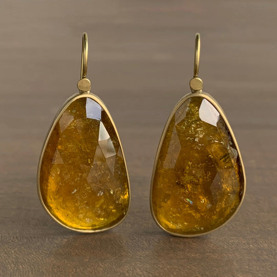 Pair of gold earrings with amber-colored teardrop stones on a brown background