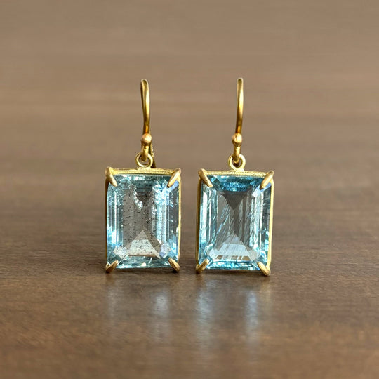 Gold earrings with rectangular blue gemstones on a brown background