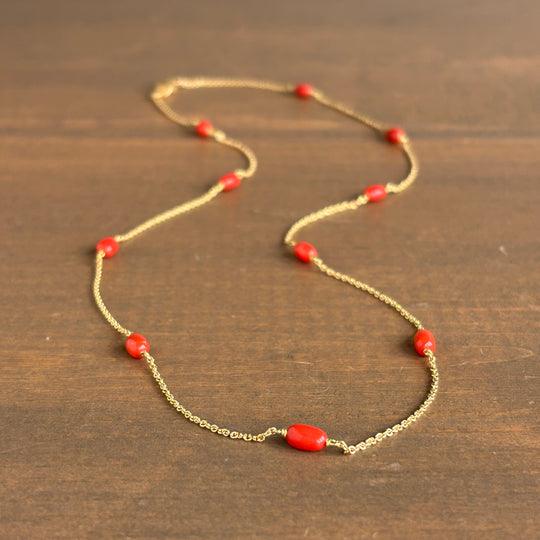 A delicate gold chain necklace with small red beads, displayed on a dark brown wooden surface.
