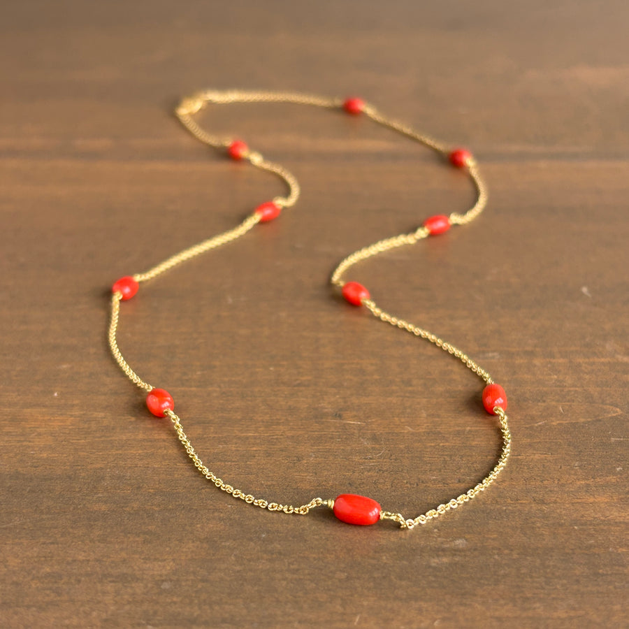 A delicate gold chain necklace with small red beads, displayed on a dark brown wooden surface.