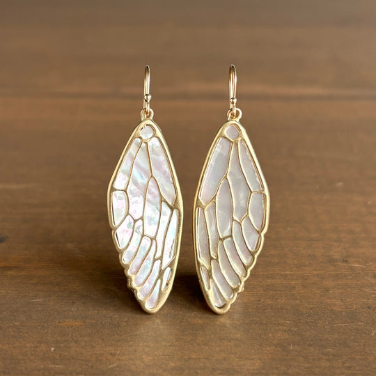 Gold wing-shaped earrings on a wooden surface