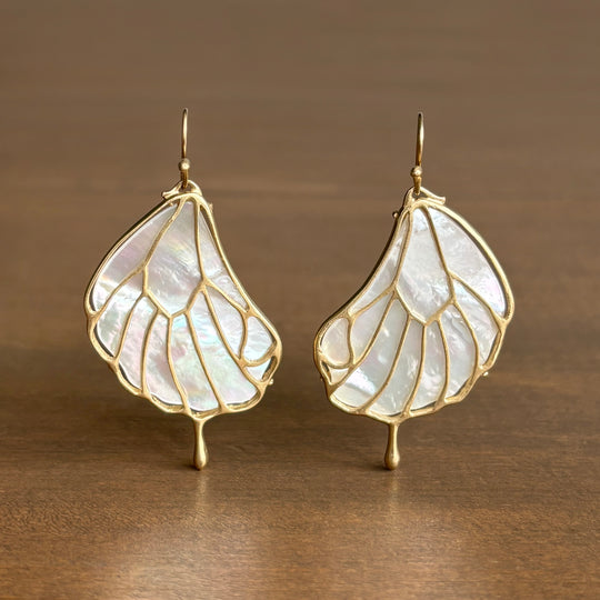 Pair of leaf-shaped earrings with gold frames on a wooden surface