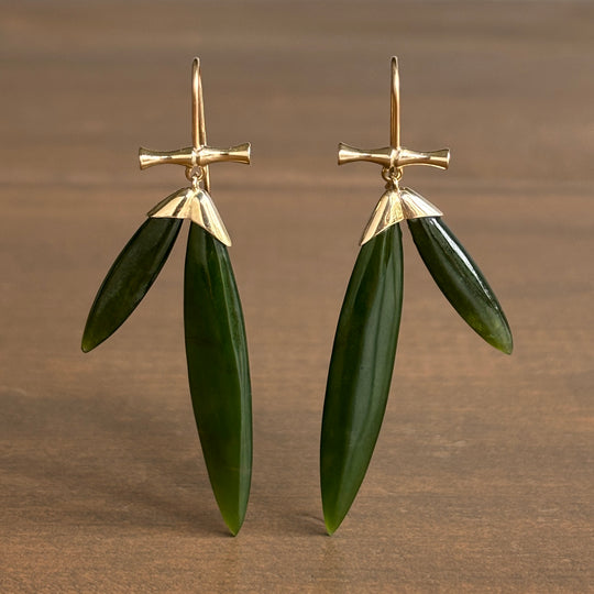 Gold and green leaf-shaped earrings on a brown background