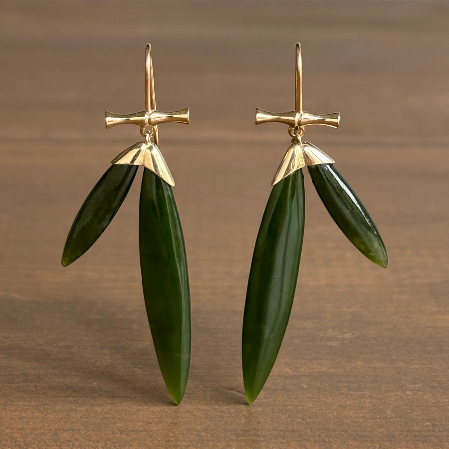 Gold and green leaf-shaped earrings on a brown background