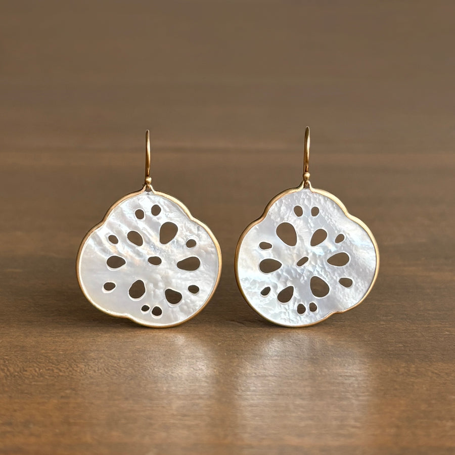 Pair of gold and white earrings on a wooden surface