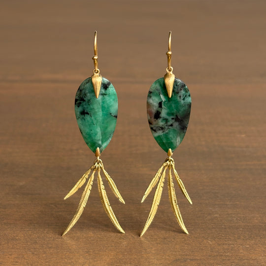 Pair of earrings with green gemstones and gold accents on a wooden background