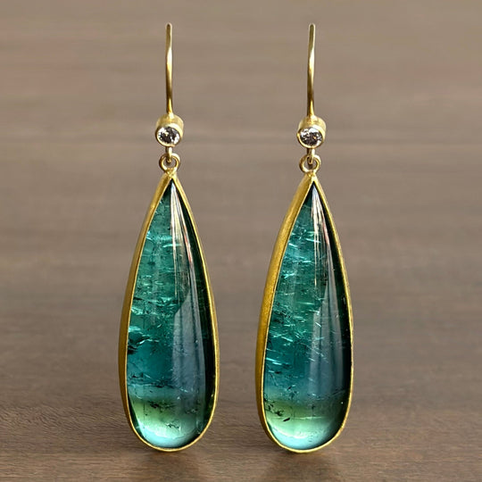 Teardrop-shaped green gemstone earrings with gold frames on a brown background