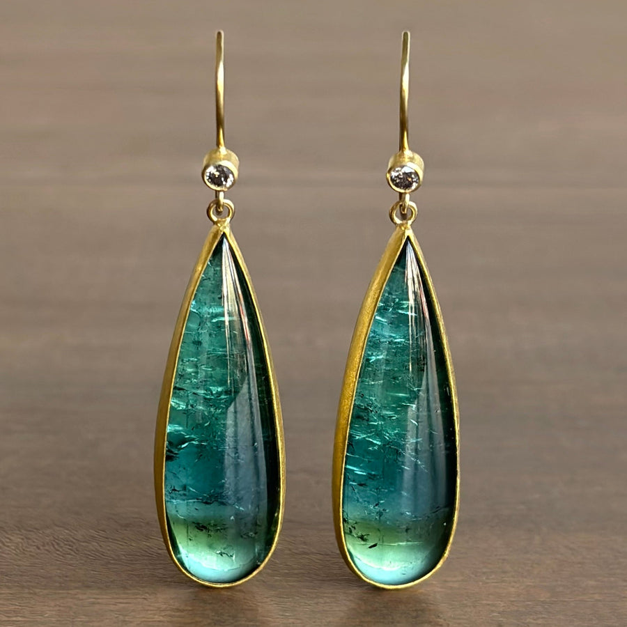 Teardrop-shaped green gemstone earrings with gold frames on a brown background