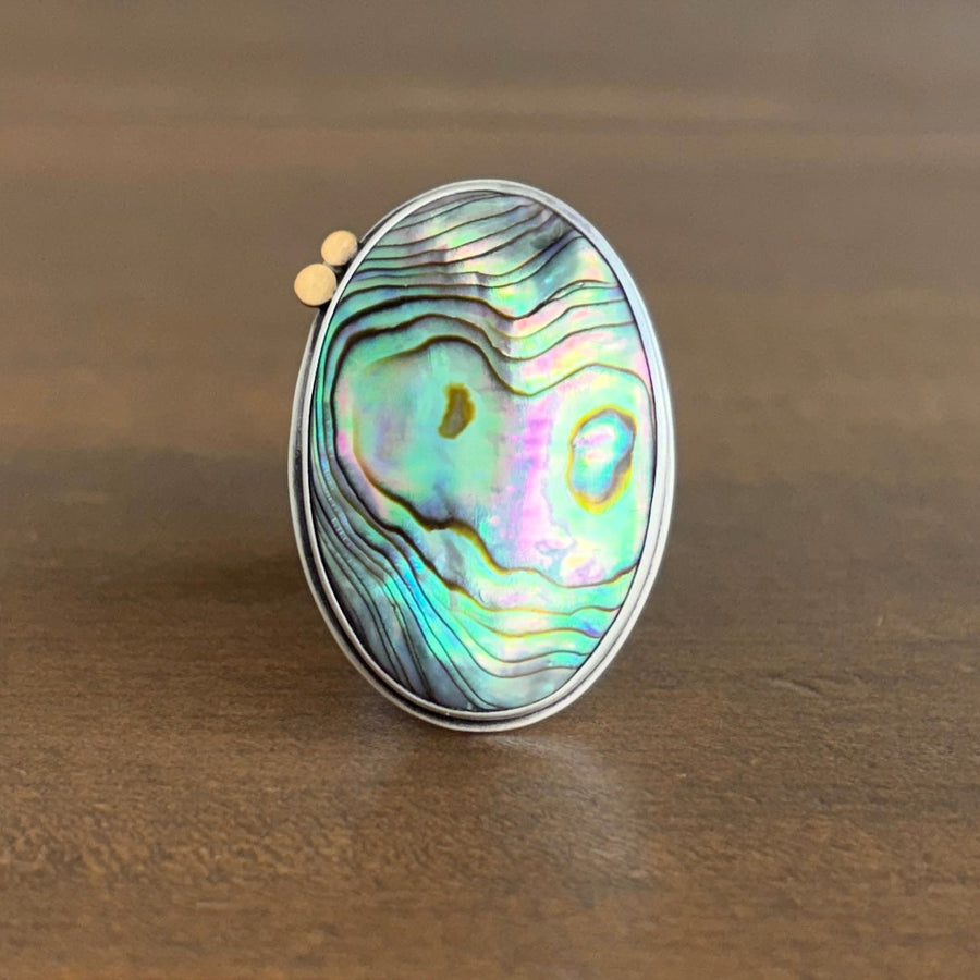 Ring with abalone shell inlay on a wooden surface