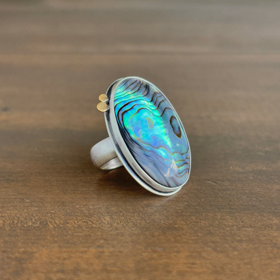 Ring with abalone shell inlay on a wooden surface