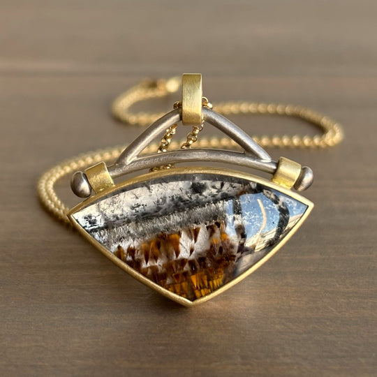 Gold and silver pendant with a textured design on a brown surface