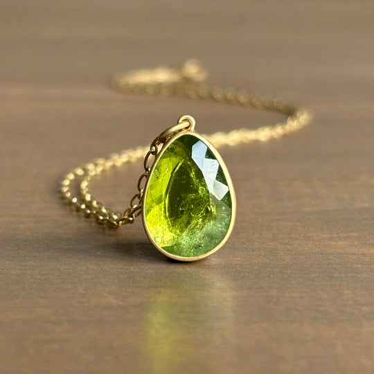 Green teardrop pendant on a gold chain against a wooden background